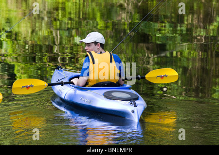 Un giovane ragazzo caucasico in un kayak con giubbotto salvagente e attrezzi da pesca. Foto Stock