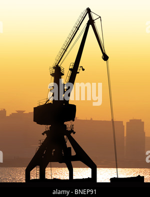 Gru sit drammaticamente contro un tramonto colorato in un cantiere di grandi dimensioni Foto Stock