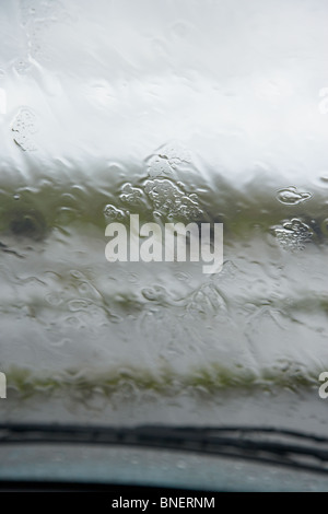 Guardando fuori attraverso il parabrezza auto a pioggia caduta sul vetro durante l'estate in Regno Unito Irlanda Foto Stock