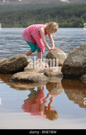 Una giovane ragazza bionda in un top rosa e turchese leggings paddling sulle rive di Loch Morlich vicino a Aviemore Inverness-shire Foto Stock