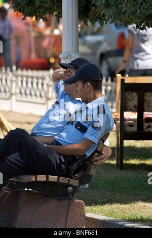 Due polizia turca (Polis) ufficiali in appoggio all'ombra su un parco di legno al banco con i passanti in background in Istanbul Foto Stock