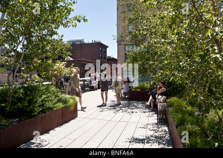 Persone pausa per guardare al di sopra della ringhiera in strade o sedersi all'ombra di alberi di ricovero alla punta meridionale della città di New York High Line Park Foto Stock