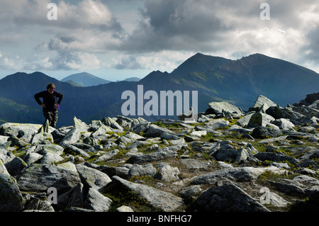 Un centro di età walker raggiunge la cima del Glyder Fach/Fawr cresta con le cime del monte Snowdon gamma in background. Foto Stock