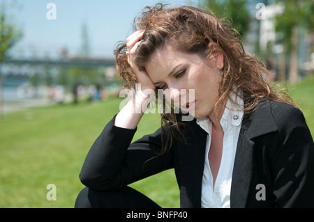 Giovani preoccupati business donna posa all'aperto in erba - testa in mano Foto Stock