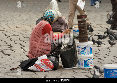 Due donne con headscarfs vendere il grano per i passanti per alimentare i numerosi piccioni, di fronte al Grand Bazaar, Istanbul Foto Stock