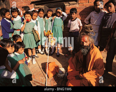 Allievi di Patan, Nepal, raccogliersi attorno a un Indù uomo santo o saddhu Foto Stock