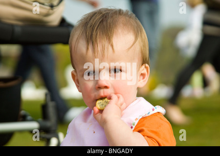 Chiudere orizzontale su ritratto di un ragazzino seduto fuori ad un picnic di mangiare un cracker o biscotto. Foto Stock