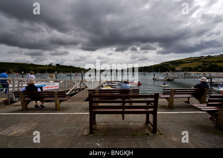 Salcombe Harbour e la foce in un cupo giorno. Un paio di persone di sedere sulle panchine a guardare il porto su una mattina nuvoloso. Foto Stock