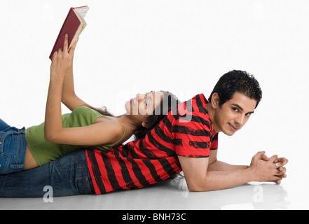 Donna sdraiata su un uomo della schiena e la lettura di un libro Foto Stock