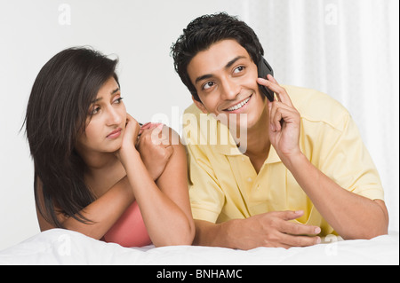 Uomo che parla di un cellulare con una donna che guarda triste accanto a lui Foto Stock