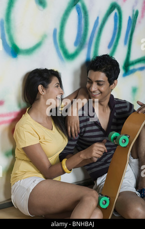 Giovane seduto con uno skateboard nella parte anteriore di un coperto di graffiti wall Foto Stock