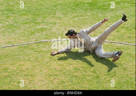 Imprenditore immersioni subacquee per fermare una palla vicino alla linea di confine in un campo di cricket Foto Stock