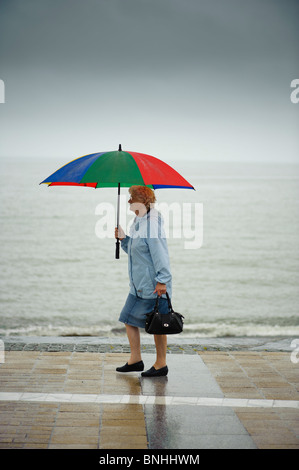 Una donna che cammina lungo Aberystwyth promenade sotto la pioggia su un luglio bagnato estate pomeriggio, Wales UK Foto Stock