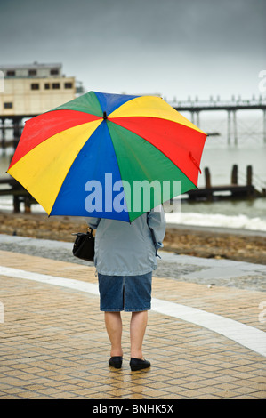 Vista posteriore di una donna il ricovero sotto un ombrellone in Aberystwyth promenade sotto la pioggia luglio bagnato estate pomeriggio, Wales UK Foto Stock