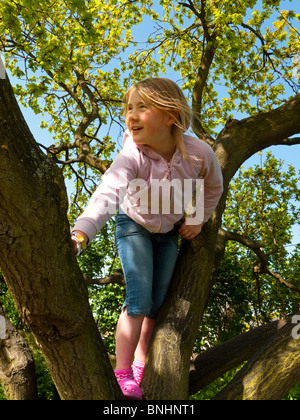 Otto anni ragazza bionda sale su un albero jeans blu e una rosa di vello alto Foto Stock