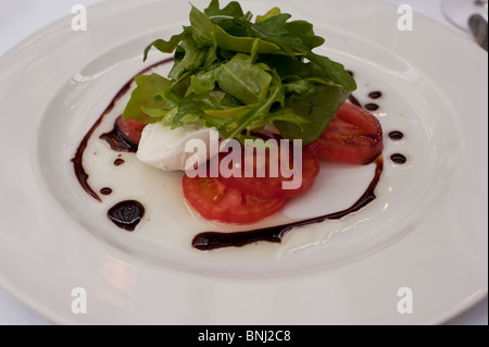 Pomodori freschi maturi servita con mozzarella di bufala, rucola, sono vestiti con una riduzione di aceto balsamico e olio d'oliva. Foto Stock
