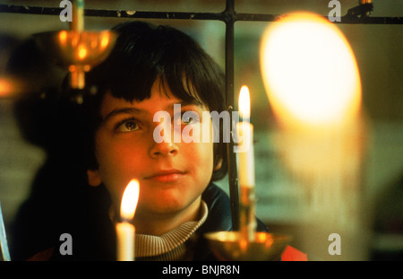 Ragazzo giovane staring al lume di candela durante il servizio in chiesa Foto Stock