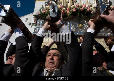 Gli uomini sollevare un trono pesanti che trasportano la Vergine del Carmen durante una PASQUA SETTIMANA SANTA PROCESSIONE in Prado del Rey, Cadiz, Spagna Foto Stock