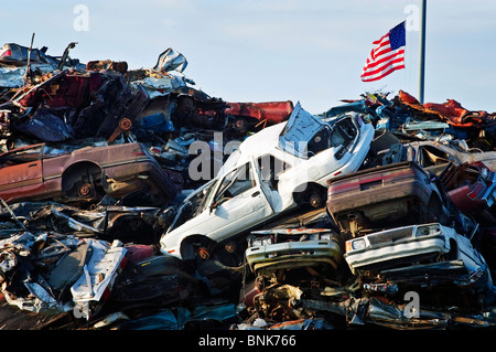 Una bandiera americana vola sopra una pila di gigante di frantumato di automobili in attesa di essere riciclato. Foto Stock