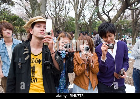 Alla moda di giovani adolescenti di scattare le foto con le fotocamere compatte digitali a Yoyogi Park, Shibuya, Tokyo, Giappone Foto Stock