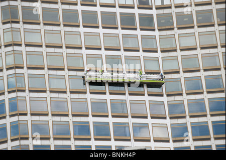 Detergenti per finestre su un gantry pulire il vetro di un centro della città edificio per uffici Foto Stock