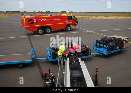 Servizi in aeroporto un camion dei pompieri e gestore di bagaglio carico di sacchi da un carrello su un aereo a Beziers Aeroporto Internazionale UE Foto Stock