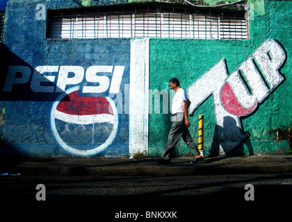 Un uomo cammina passato soft drinks pubblicità su una parete in Santo Domingo, Repubblica Dominicana Foto Stock