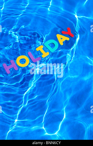 La parola vacanza fatta da lettere di schiuma galleggiante sulla superficie dell'acqua di piscina Foto Stock