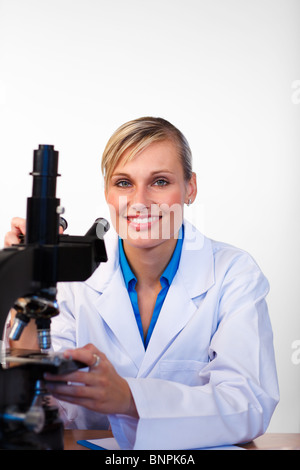 La bionda di scienziato con un microscopio a sorridere alla telecamera in un laboratorio Foto Stock