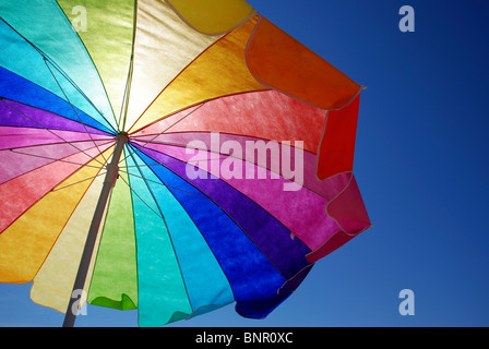 Color arcobaleno ombrellone in spiaggia contro il cielo blu e chiaro. Foto Stock