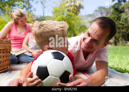 Padre e figlio in possesso di un pallone da calcio con la loro famiglia lettura in background Foto Stock