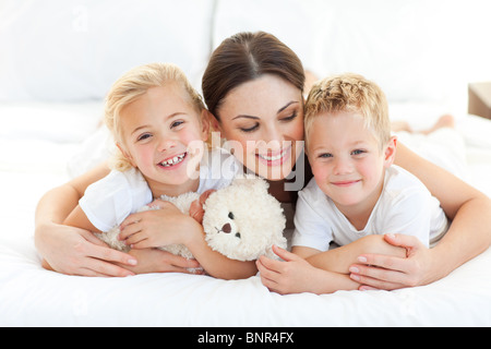 Allegro i bambini con la loro madre giacente su un letto Foto Stock