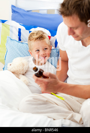 Bello padre dando tosse sciroppo al suo figlio malato Foto Stock