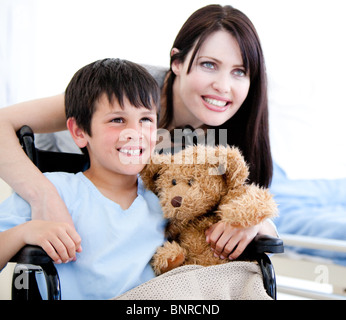 Sorridente little boy in una sedia a rotelle con sua madre Foto Stock