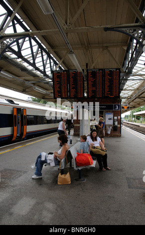 I passeggeri in arrivo e in attesa di un treno al di sotto delle partenze della scheda informazioni su Milano stazione ferroviaria in Hampshire Foto Stock