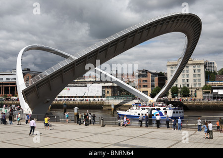 Spettatori guarda come una barca di piacere Fortuna passa attraverso l'apertura a Gateshead Millennium Bridge, England, Regno Unito Foto Stock