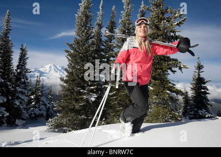 Una donna il trasporto di sci e poli escursioni nella neve con Mt. Rainier viste in background. Foto Stock