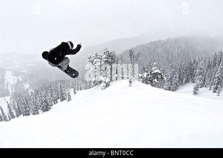 Un uomo su una snowboard vola attraverso l'aria dopo aver colpito un salto. Foto Stock