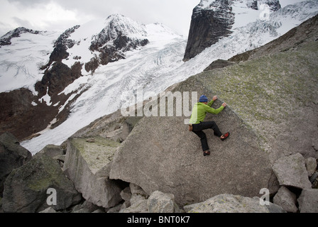 Uomo che indossa una camicia verde si arrampica su un masso di granito con grande ghiacciaio in background. Foto Stock