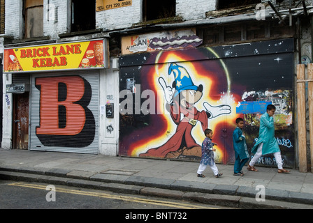 Brick Lane, a est di Londra. I figli di padre musulmano tornano dalla moschea, passando davanti a stencil Street wall art di Ben Eine e DDS. HOMER SYKES anni '2010 2010 Foto Stock