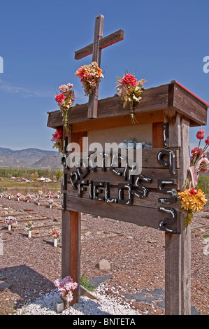 Questa immagine di stock è un vasaio nel cimitero di campo con un segno decorate con fiori artificiali e una croce contro un cielo blu. Foto Stock