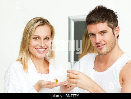 Donna che mantiene pillole e uomo con un bicchiere di succo di arancia Foto Stock