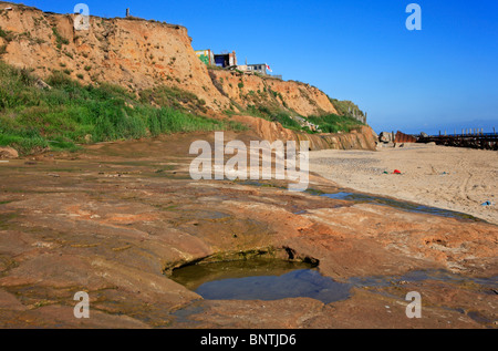 Erosione costiera a Happisburgh, Norfolk, Inghilterra, Regno Unito, con onda della piattaforma di taglio e gli edifici su cliff edge. Foto Stock
