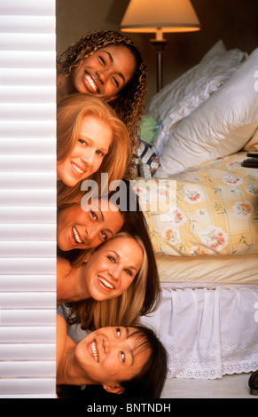 Cinque donne di mescolanza etnica impilati nella parte superiore di ogni altro a guardare fuori dalla porta della camera Foto Stock