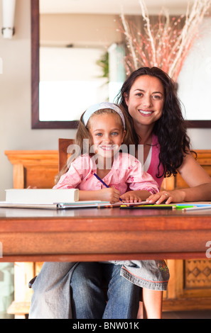 Allegro madre aiutare la propria figlia per i compiti a casa Foto Stock