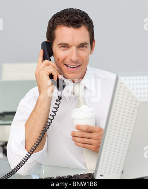 Imprenditore sorridente sul telefono di bere un caffè in ufficio Foto Stock