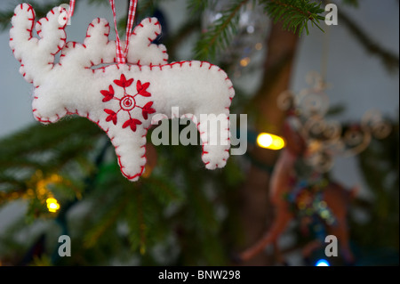Un rosso e bianco ricamato renne ornamento di Natale si blocca su un albero di abete rosso con luci colorate. Foto Stock
