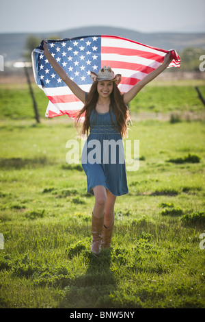 Bella cowgirl in esecuzione con bandiera americana nelle sue braccia Foto Stock