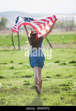 Bella cowgirl in esecuzione con bandiera americana nelle sue braccia Foto Stock