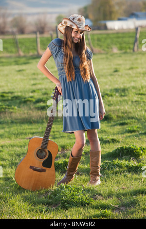 Capelli lunghi cowgirl tenendo la chitarra nel campo Foto Stock